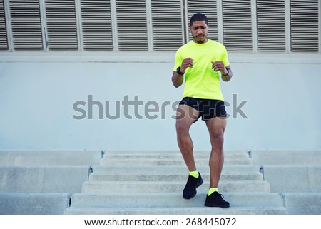 Full length portrait of sporty young man running down a flight of stairs while training outdoors at sunny afternoon,male runner dressed in bright t-shirt working out outdoors while doing legs exercise