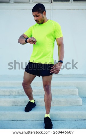 Full length portrait of male runner looking at his watch while going for a run at sunny afternoon,sporty young man dressed in bright t-shirt with space for your text message checking his time outdoors