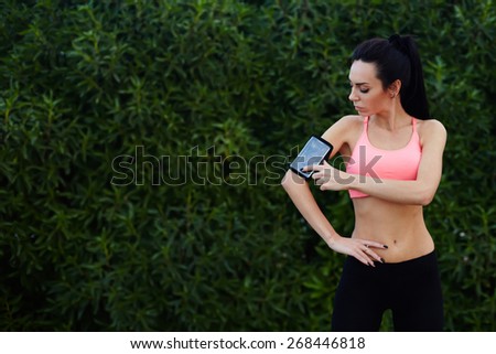 Sporty young woman standing in the park with big copy space for text while getting ready for workout,healthy fit runner setting her personal trainer application or stopwatch on cell phone before a run