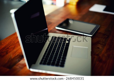 Workplace with open laptop with black screen and digital tablet on modern wooden desk, angled notebook on table in home interior, filtered image, cross process