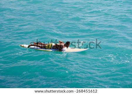 Male surfer floating on his surfboard in the waves of clean bight water, surfer man paddles out through the waves, handsome man enjoying a surf in clear blue water, sexy man surfing at the beach