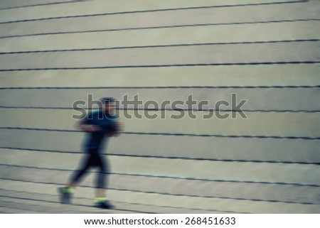 Full length portrait of athletic dark-skinned man running along beautiful grey wall outdoors, muscular build young runner working out while jogging in the park motion blur effect