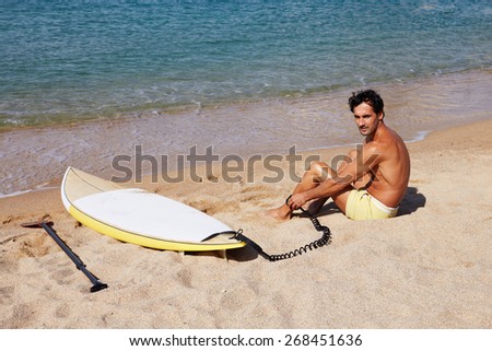 Rear view of brunette hair man sitting on the beach while enjoying good sunny day, male surfer waiting for the big waves sitting on beautiful shoreline, man seat against sea