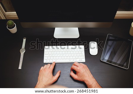 Top view of workplace with man sitting at beautiful black desk while working on pc computer, male freelancer working at home studio in modern loft, modern business concept