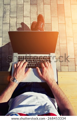 Top view male hands using notebook outdoors in urban setting while typing on keyboard, businessman freelancer working on computer while sitting on city park bench, tourist working on laptop, flare sun