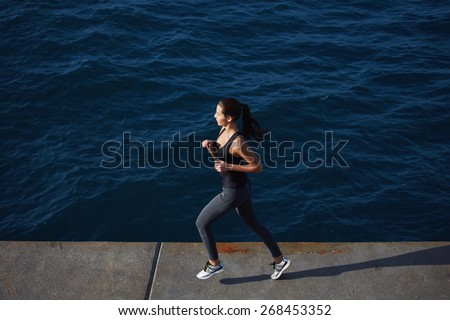 Full length portrait of a sporty young woman running along the beach with amazing big ocean waves on background