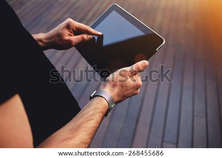 Close up male student hands using touch pad against wooden background, freelancer man working on his digital tablet with big copy space, hipster man\'s hands browsing with touchscreen device, flare