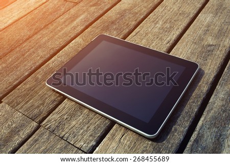 Black digital tablet with blank screen for your text message lying on wooden floor, touch pad wireless device lying on old wooden desk, flare sun light