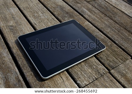 Black digital tablet with blank screen for your text message lying on wooden floor, touch pad wireless device lying on old wooden desk