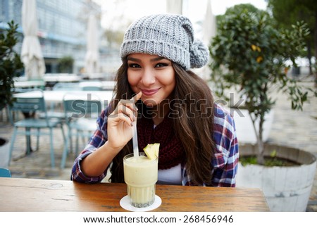 Portrait of beautiful young woman enjoying a drink, pretty girl sipping banana juice in coffee shop terrace