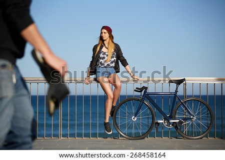 Full length portrait of stylish hipster girl standing with her sport fixed gear bike on the beach, young woman enjoying beautiful afternoon outdoors with blue sea on background, promenade at sunny day
