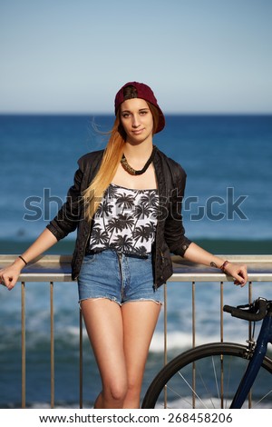 Half length portrait of stylish hipster girl standing with her sport fixed gear bike on the beach, young woman enjoying beautiful afternoon outdoors with blue sea on background, promenade at sunny day