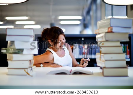 Working hard for great grades, asian smiling student girl sitting at the desk behind stack of books in university library, female teenager looking so happy with schooling, exam preparation