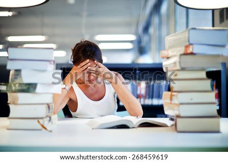 Frustrated female student sitting at the desk with a huge pile of study books in university library, young asian college student at hard exam preparation in study hall looking tired and weary