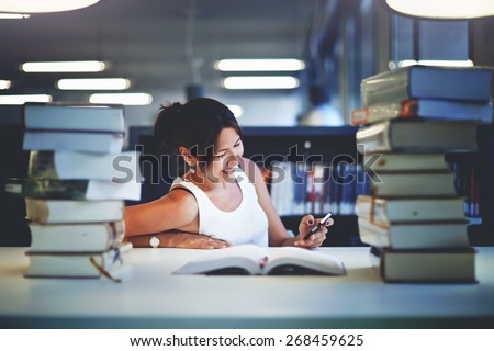 Working hard for great grades, asian smiling student girl sitting at the desk behind stack of books in university library, female teenager looking so happy with schooling, exam preparation