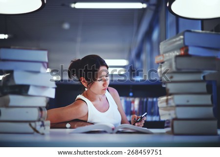 Frustrated female student sitting at the desk with a huge pile of study books in university library, young asian college student at hard exam preparation in study hall looking tired and weary