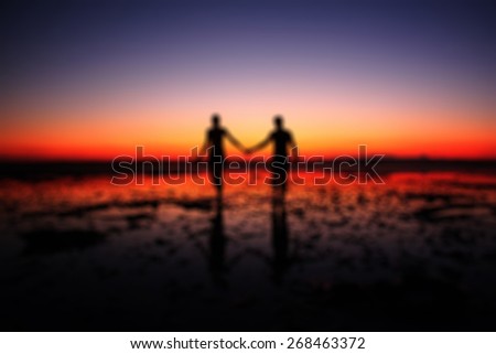 Amazing bokeh silhouette of couple walking hand in hand on sunset background, two people in love walking on the beach blur effect