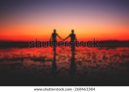 Bokeh Silhouette of young couple in love holding hands at sunset at the seaside, two people in love walking on the beach blur effect