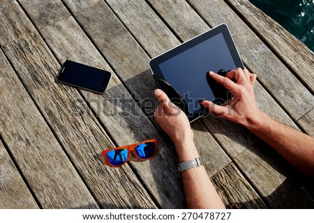 Top view male hands using digital tablet on wooden jetty background, vacation holidays concept, lying smart phone, colorful sunglasses and mans hands with touch pad