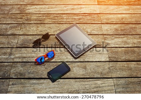 Top view mock up presentation with blank screen digital tablet, smart phone and couple of sunglasses lying on the wooden texture, vacation holidays or recreation time concept, flare sun light