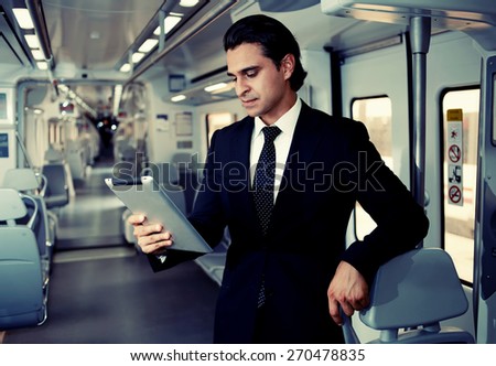 Successful mature businessman using digital tablet on the way to work in train, male executive reading news or digital book in public transport interior, handsome entrepreneur use touch pad for work