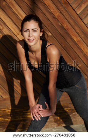 Smiling young female runner stretching her muscles before a training session outdoors, sporty woman warming up before a workout, brunette hair pretty girl doing stretching legs exercise outside