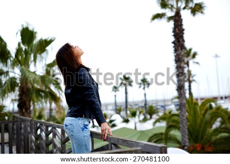 Side view shot of brunette young woman breathing fresh air and enjoying the view just arrived to hotel, attractive female enjoying the view while standing on the balcony during her vacation holidays