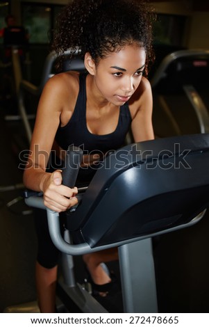 Portrait of focused afro american girl working out on bike at gym