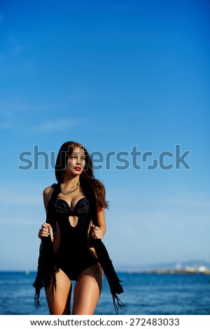 Sexy young woman in bikini posing on blue sea and sky background, fashion model with perfect make up and beautiful figure standing on the beach, female enjoying sunny afternoon and her summer holidays