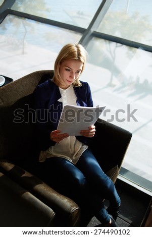 Top view portrait of young attractive businesswoman examining paperwork in bight light office interior sitting next to the window, business woman read some documents before meeting