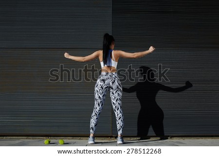 Back view portrait sporty woman with perfect figure and buttocks stretching her arms against wall with copy space for your text message,fit female in sportswear exercising on black background outdoors