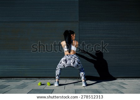 Rear view sporty woman with perfect figure and buttocks doing squats against wall with copy space for your text message,fit female in sportswear squatting after training on black background outdoors