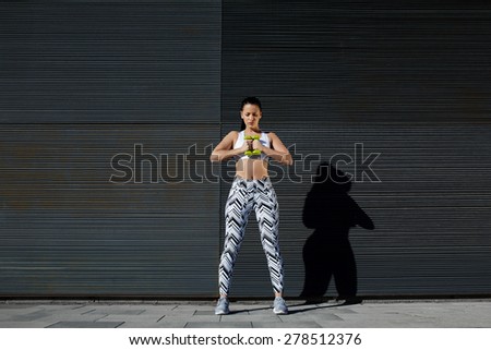 Focused sporty woman using dumbbells to work out her arms while training outdoors against black copy space wall for your text message, female in workout gear holding weights with her hands together