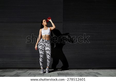Healthy fit woman with perfect figure wearing sports workout clothing, female runner drink while take breaking after fitness training in urban setting, space for your text message, body shape buttocks