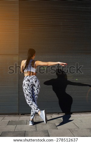 Sporty woman with perfect figure and buttocks shape exercising against wall with copy space for your text message, fit female in sportswear working out on black background outdoors, flare sun light