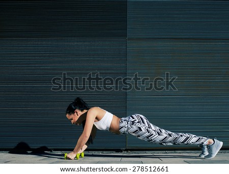 Healthy young woman doing press ups with dumbbells on black background outdoors, female in workout gear doing push-ups with some weights against wall with copy space for your text message, filter