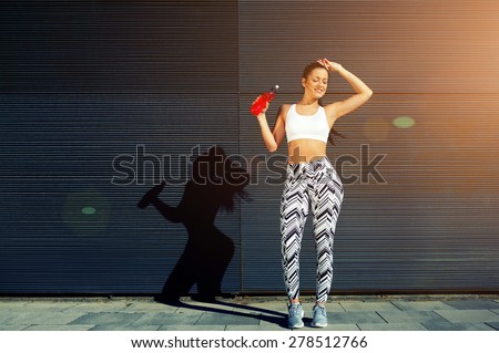 Female runner hold energy drink bottle standing against black wall background with space for your text message, athletic woman resting after fitness training outdoors in the city, happiness concept