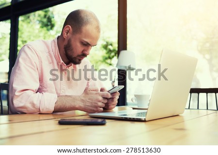 Young freelancer use smart phone sitting in modern loft interior with big windows, business man text messaging at office desk, male student sitting at wooden table of modern university library, filter