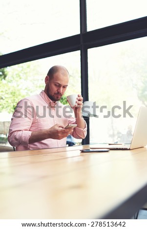 Modern business man connecting to wireless on his smart phone during coffee break, male freelancer reading text message oh cell phone while working in loft studio, university student working at cafe