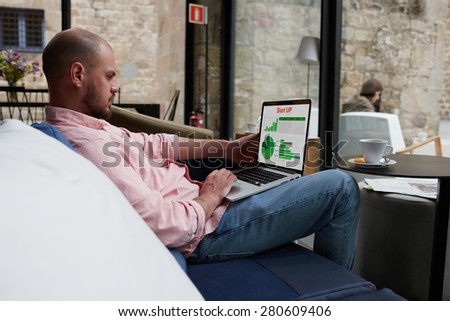 Businessman sitting front laptop computer with financial information as graphics and charts on screen, young entrepreneur working with statistics data and analyzing performance on his notebook