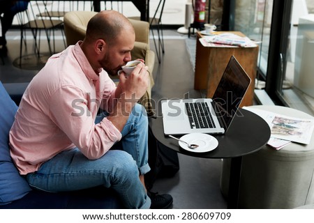 Experienced businessman sitting front laptop computer with blank screen copy space for your content, young student work on notebook holding cup of tea or cafe while he sitting in modern coffee shop