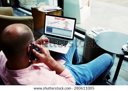Young businessman sitting front laptop computer with financial information as graphics and talk on smart phone, entrepreneur busy work with statistics data discussing performance via mobile phone call