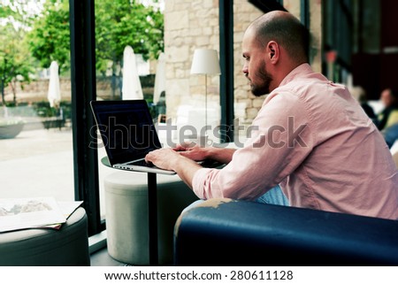 Successful businessman sitting front open laptop computer with blank screen for your content, young freelancer work on notebook in modern coffee shop or hotel interior, make money on-line, e-business