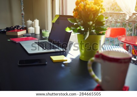 Freelancer needs workstation, workplace with open laptop computer, smart phone, notebook, cup and pot of flowers, on-line learning or distance work concept, modern table at window in home interior