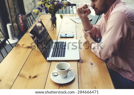 Male freelancer connecting to wireless via laptop computer, thoughtful businessman work on notebook while sitting at wooden table in modern coffee shop interior, student reading text or book in cafe