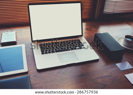 Laptop computer with white blank copy space screen for text message or publicity content lying on wooden table with digital tablet and stylish accessories,electronic business and distance work concept