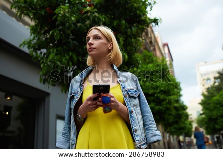 Young woman hold smart phone standing on mandarin tree background in the city, lost female tourist using telephone for navigation checking out the sights,student girl browsing internet on mobile phone