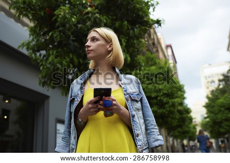 Young woman hold smart phone standing on mandarin tree background in the city, lost female tourist using telephone for navigation checking out the sights,student girl browsing internet on mobile phone