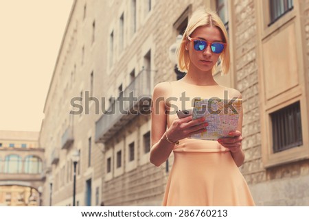 Young female tourist checking out the sights while reading a map, gorgeous woman holding a map while touring abroad, stylish hipster studying a map while standing in urban setting in summer, filter