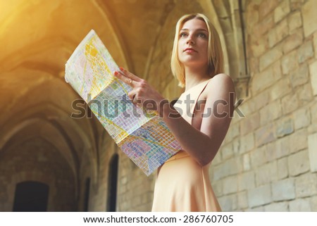 Portrait of young female tourist checking out the sights while reading a map, gorgeous woman holding a map while touring abroad,stylish hipster studying a map while standing in antique town in summer